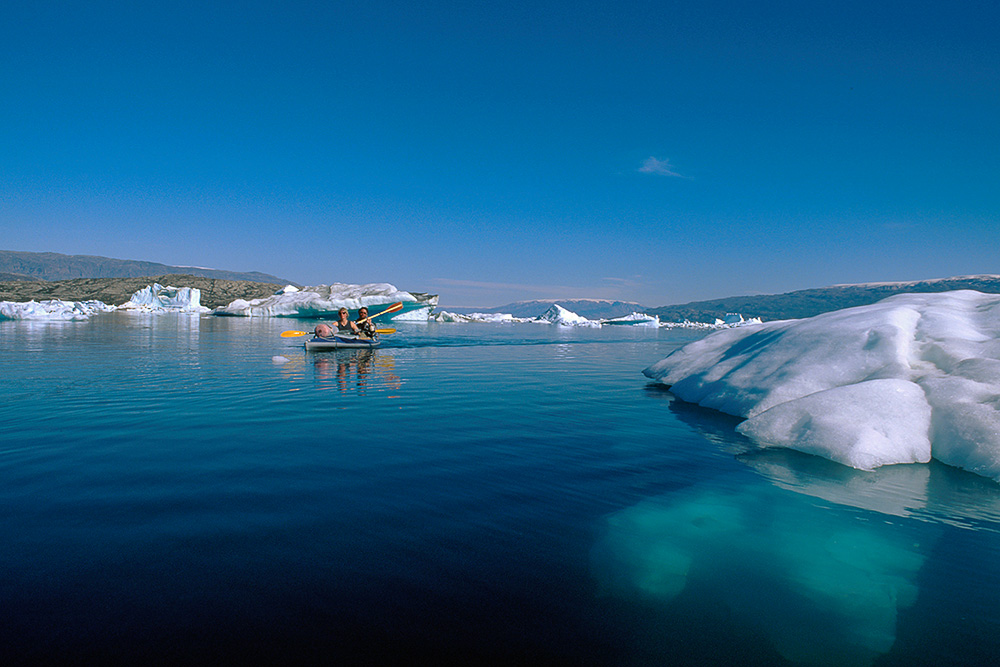 Kajakpaddlare i Rödefjord. Isberg, blå himmel och klart, blått vatten, östra Grönland.