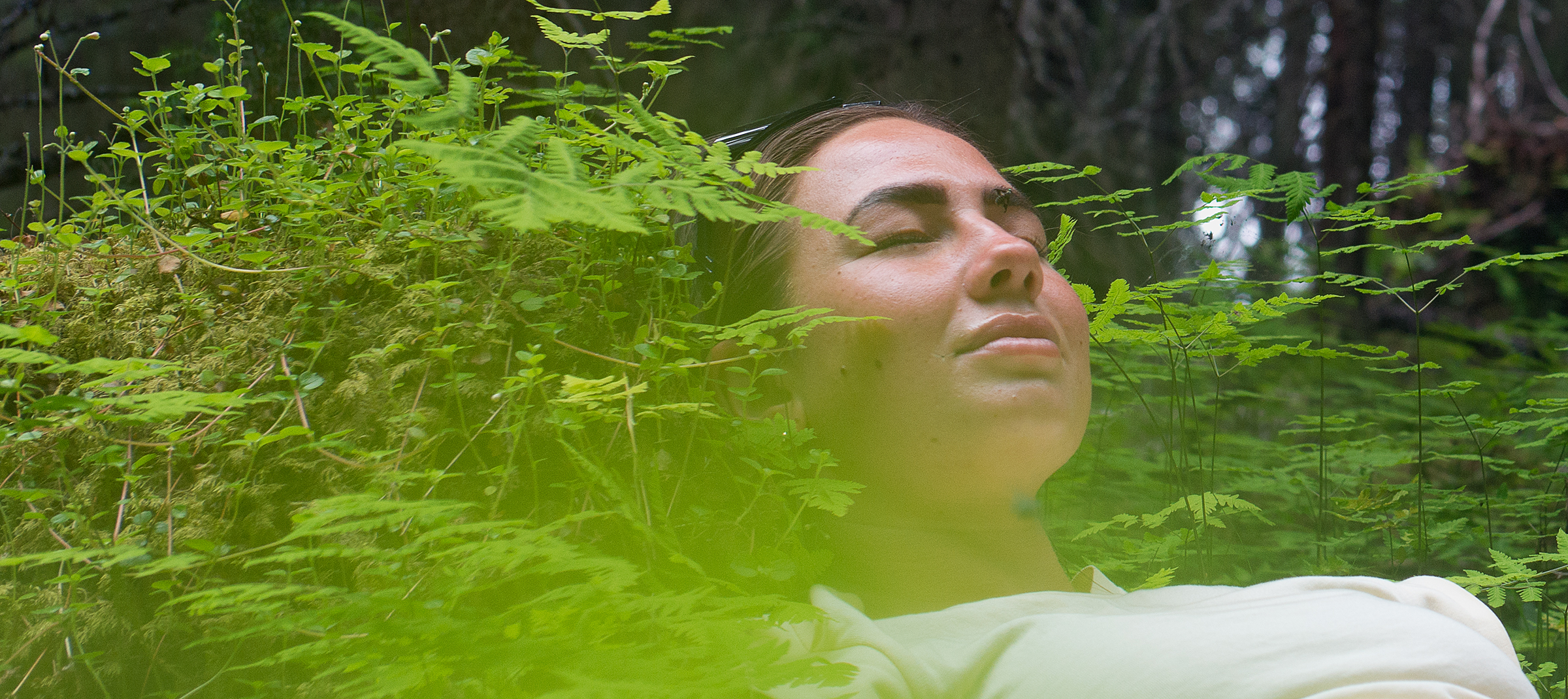 Ung kvinna vilar i grönskan i en skog, hon skogsbadar.